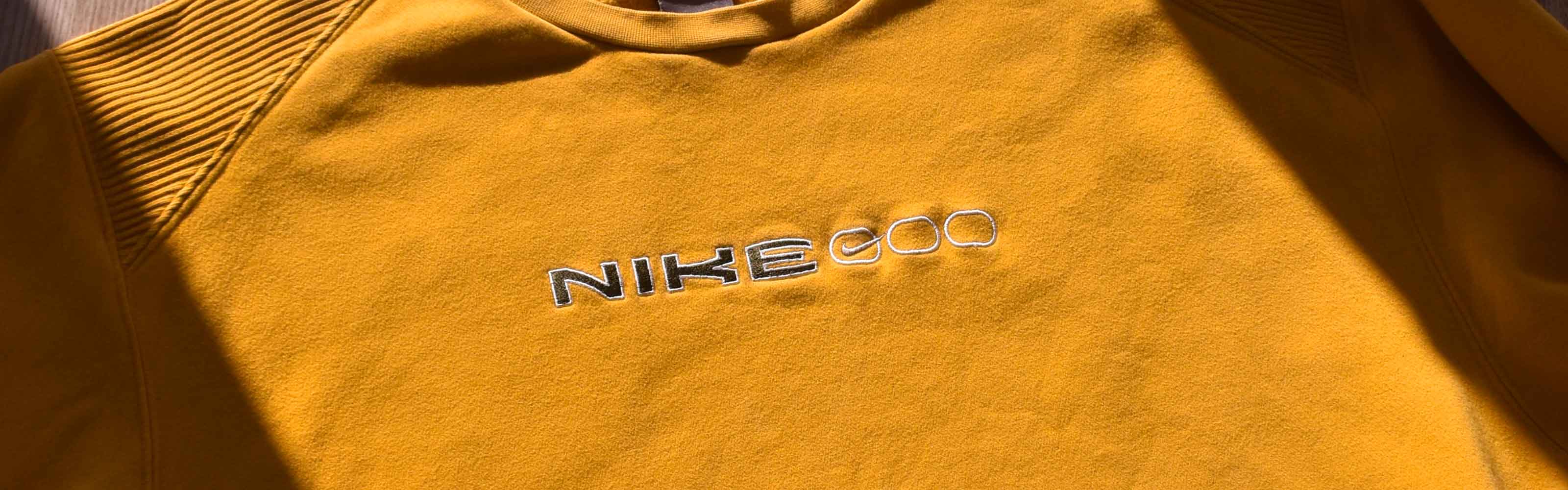 Yellow Nike sweatshirt with intricate embroidery, casually placed on the ground